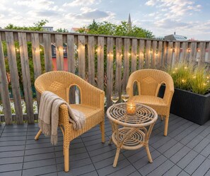 A wooden deck with wicker furniture, including two chairs and a small table with a candle and glasses. - Perfectly Situated: Downtown Luxury Loft (Reykjavík)