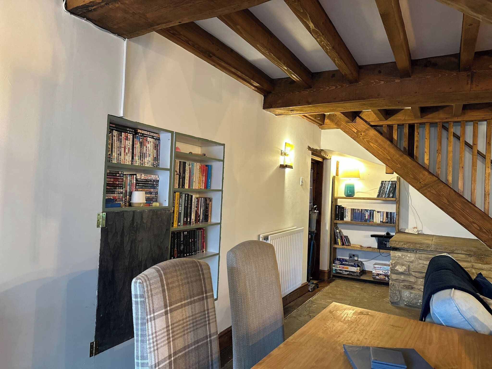 A cozy room with a wooden ceiling, a bookshelf filled with books, a plaid chair, and a table.