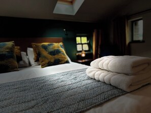 Cama bem arrumada com toalha branca dobrada, manta estampada e dois travesseiros decorativos.