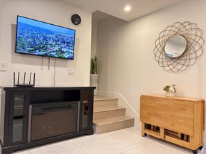 Un salon moderne avec un téléviseur à écran plat fixé au mur, un meuble de rangement sombre, un buffet en bois et un escalier menant à l’étage supérieur.