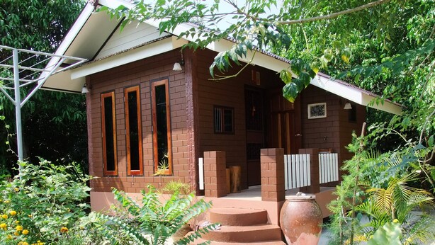 A small brick house with a porch, surrounded by various plants and a large pot. - Bansuan Banjong Akkson (Klaeng)