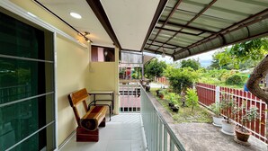 A balcony with a wooden bench, potted plants, and a view of a garden. - Bansuan Banjong Akkson (Klaeng)