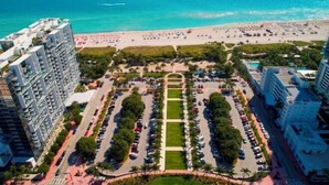 Een hoog hotel met een centrale binnenplaats, een strand en een parkeerplaats.