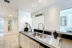 A modern kitchen with a stainless steel sink, a coffee maker, and a built-in window with a decorative grid. - Casagrandesouthbeach by AmericanVacationLiving 4Rm (Miami Beach)