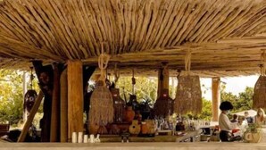 A rustic outdoor seating area with a thatched roof, wooden pillars, and hanging decorations.