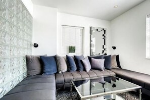A modern living room with a dark leather sofa, a glass coffee table, and a patterned wall. - Casagrandesouthbeach by AmericanVacationLiving 4Rm (Miami Beach)