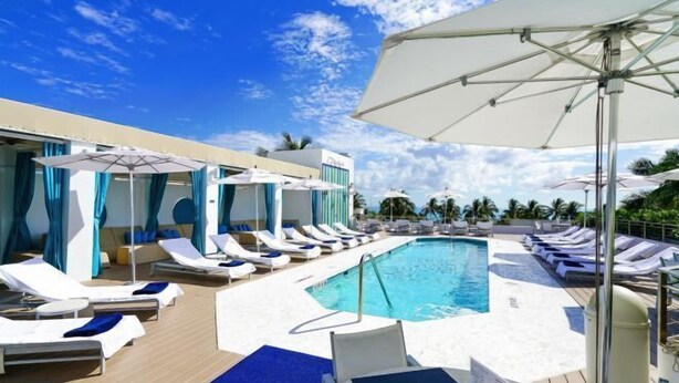 Un espace aménagé au bord de la piscine, avec des chaises longues, des parasols et un ciel d’un bleu limpide.