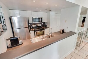 A modern kitchen with stainless steel appliances, white cabinetry, and a central island with a sink. - Casagrandesouthbeach by AmericanVacationLiving 4Rm (Miami Beach)