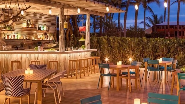 Un'area bar all'aperto con tavoli e sedie in legno, un bancone bar e una struttura a pergola.