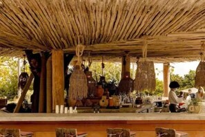 A rustic outdoor seating area with a thatched roof, wooden tables, and hanging decorations. - Casagrandesouthbeach by AmericanVacationLiving 4Rm (Miami Beach)