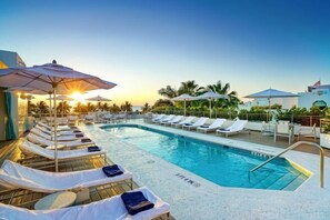 A poolside area with sun loungers and umbrellas, a clear sky, and palm trees in the background. - Casagrandesouthbeach by AmericanVacationLiving 4Rm (Miami Beach)