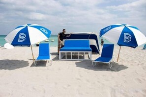 A beach setting with two blue and white umbrellas, a table, and lounge chairs. - Casagrandesouthbeach by AmericanVacationLiving 4Rm (Miami Beach)