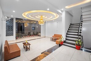A modern lobby with a sofa, coffee table, chandelier, staircase, and potted plants. - Shree Sita Sadan (Faizabad)