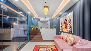 Eine moderne Hotellobby mit einem Marmor-Rezeptionsschalter, einem rosafarbenen Sofa mit floralen Kissen, einer Kristallleuchtre und einer Wand mit Statuen.