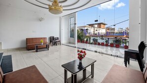 Ein geräumiger Raum mit großem Fenster, einem braunen Sofa, einem kleinen Tisch mit Blumenvase und einer Kandelaber.