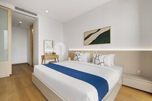 Ett modernt hotellrum med en stor säng, ett sängbord, en liten avlastningsyta och ett konstverk som hänger på väggen.