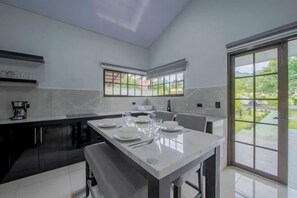 A modern kitchen with a dining area, large windows, and a view of the outdoors. - Villa Escondida La Fortuna (La Fortuna)