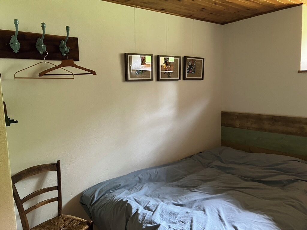 A bedroom with a bed, a wooden headboard, a chair, and three framed pictures on the wall.