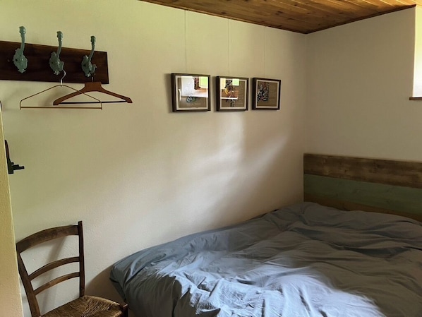 A bedroom with a bed, a wooden headboard, a chair, and three framed pictures on the wall.