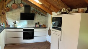 Una cocina con horno integrado, armarios blancos, un refrigerador blanco y ollas de cobre colgando.