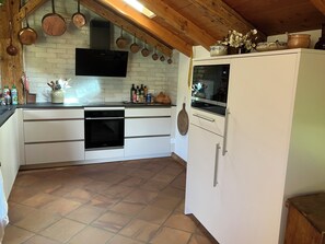 A kitchen with a built-in oven, white cabinets, a white refrigerator, and hanging copper pots.