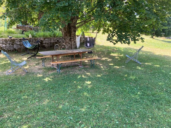 A picnic setup with a wooden table, benches, and a hammock under a tree.