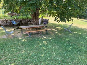 Un'area picnic con tavolo in legno, panchine e un'amaca sotto un albero.