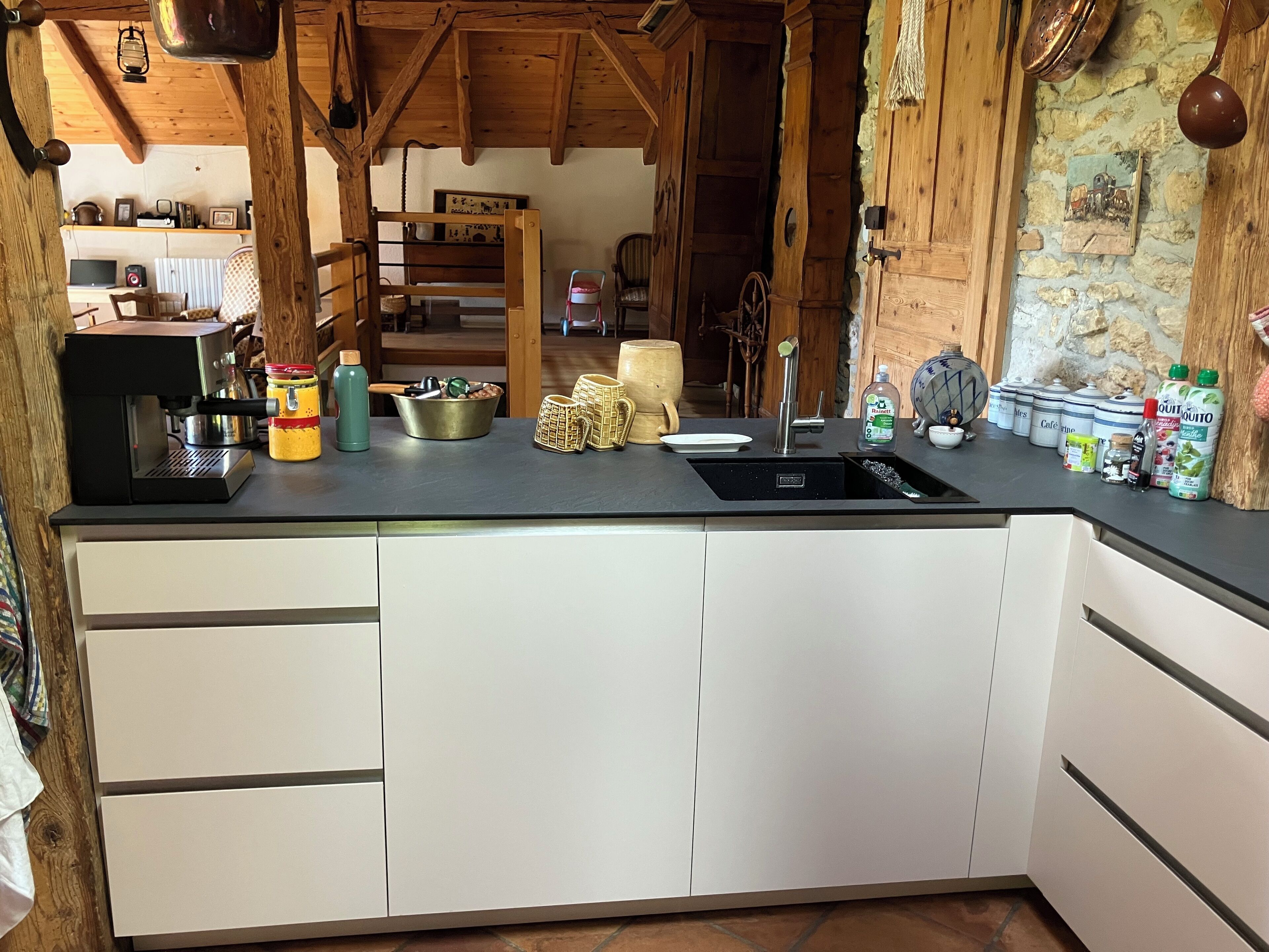 A kitchen with a black countertop, white cabinets, and a sink. There are various kitchen items like a coffee maker, jars, and a kettle.