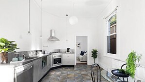 A modern kitchen with stainless steel appliances, a dining area with a glass table, and a view of the garden through a window. - Prime home near train, trams, cafes, schools, Yarra River & city attractions (Richmond)