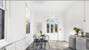 A kitchen with a dining area, white walls, and a tiled floor. - Prime home near train, trams, cafes, schools, Yarra River & city attractions (Richmond)