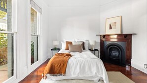 A bedroom with a large bed, a fireplace, and a view through a window. - Prime home near train, trams, cafes, schools, Yarra River & city attractions (Richmond)