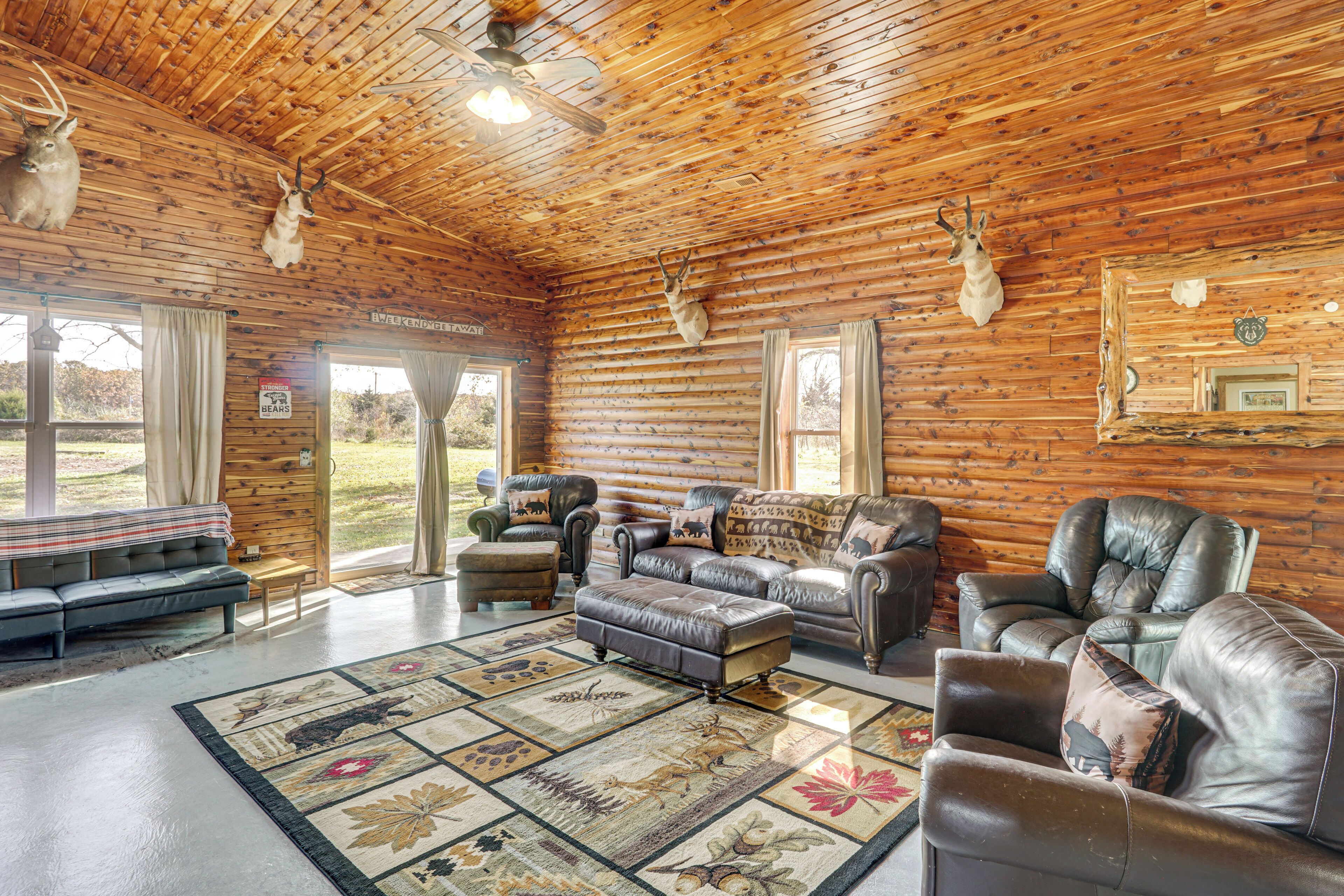 A log cabin interior with leather furniture, a large rug, and mounted animal heads on the walls.