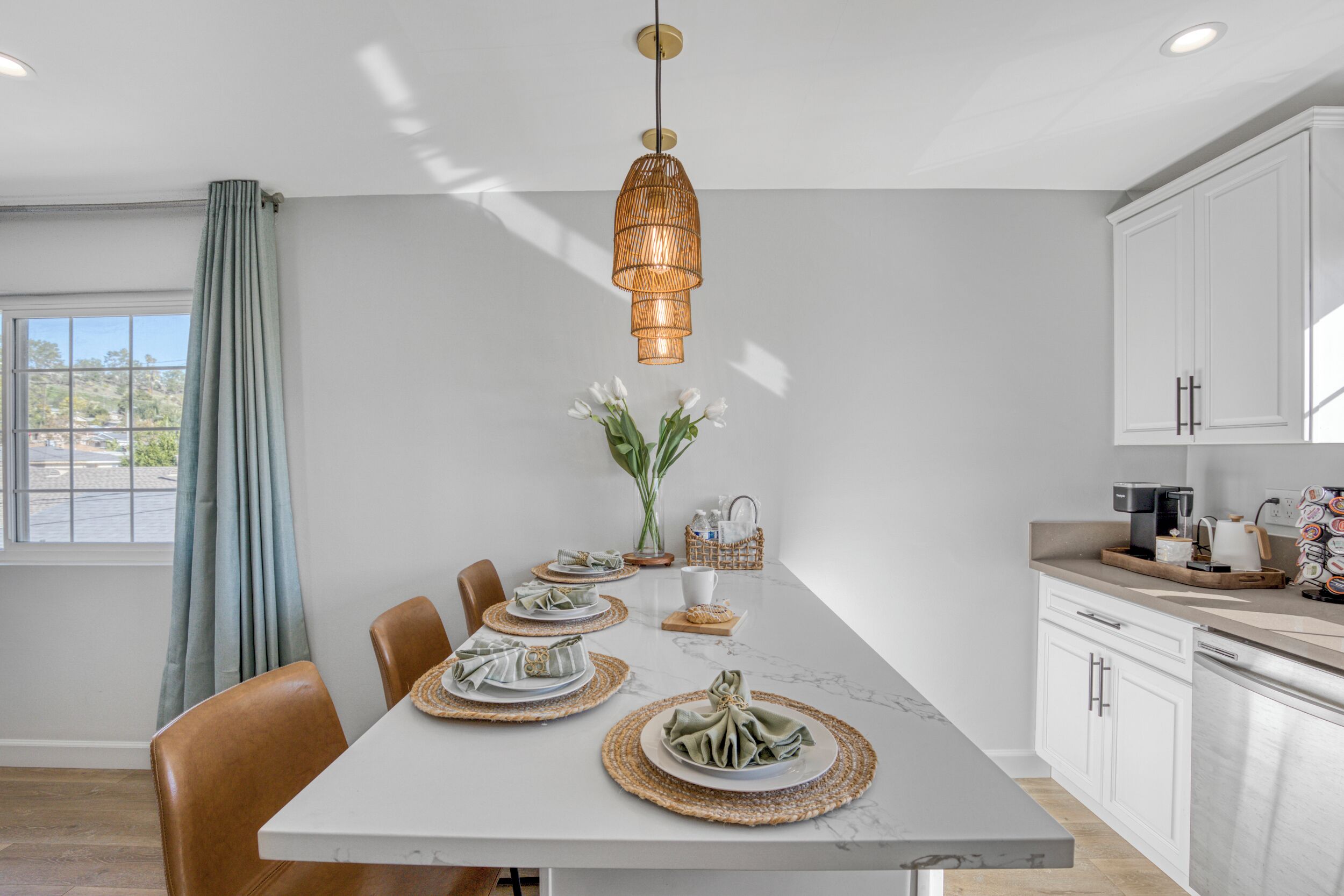 A modern kitchen with white cabinets, a marble countertop, and a dining table set for four.