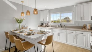 Uma cozinha moderna com armários brancos, uma ilha grande com banquetas, iluminação pendente e vista pela janela.
