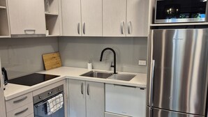 Une cuisine moderne avec des meubles blancs, un réfrigérateur en acier inoxydable, un four encastré et un robinet noir.