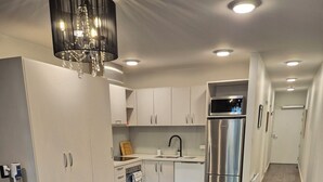 Une cuisine compacte avec des meubles blancs, un réfrigérateur en acier inoxydable et un lustre moderne.