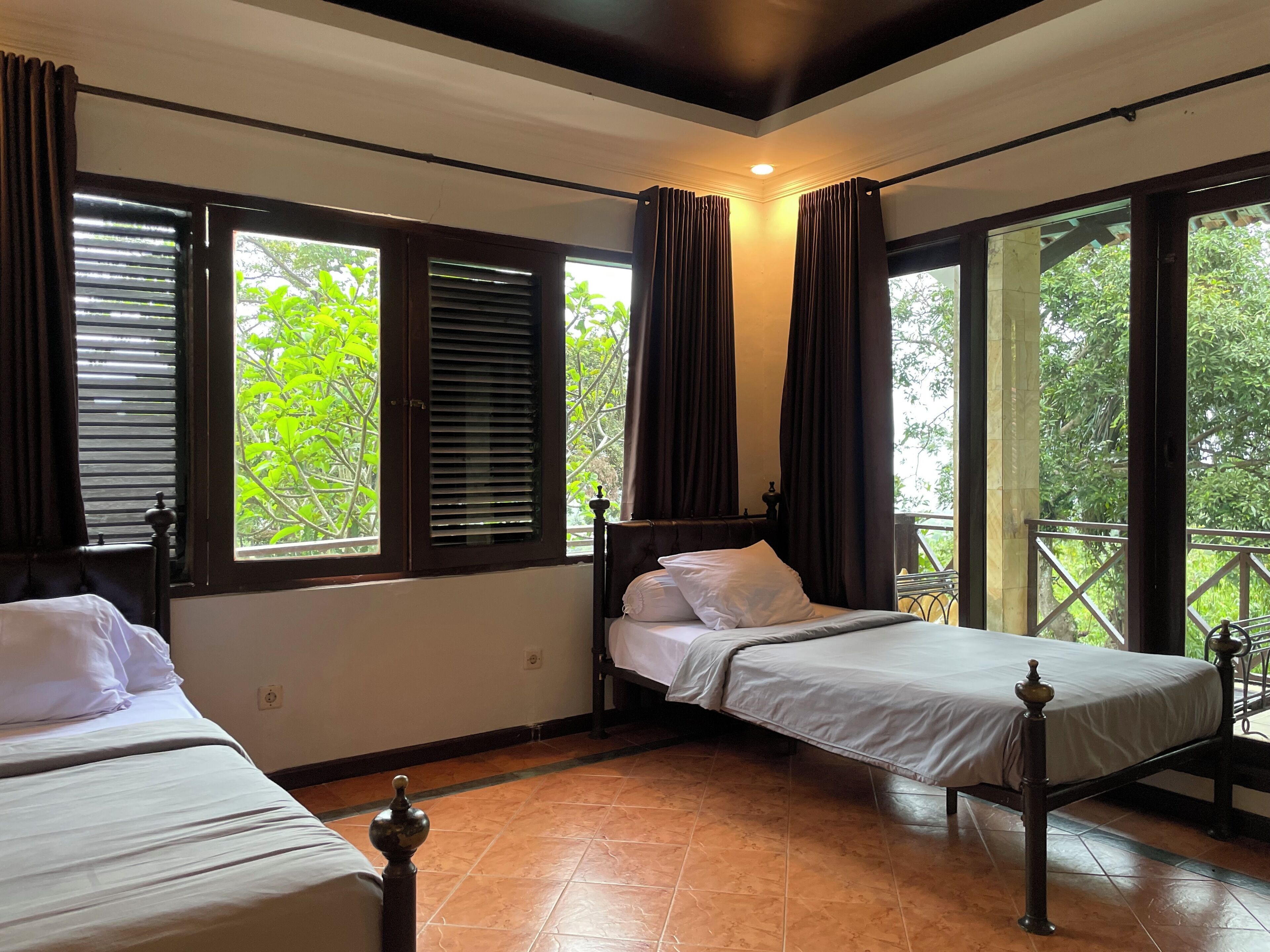Una habitación con dos camas, ventanas amplias con cortinas, suelo de baldosas y una lámpara en el techo.