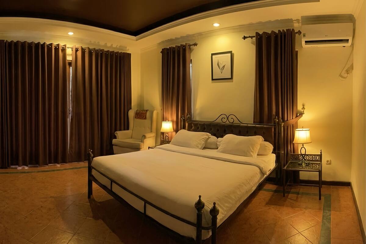 A hotel room with a large bed, two bedside tables with lamps, a flat-screen TV, and a large window with curtains.