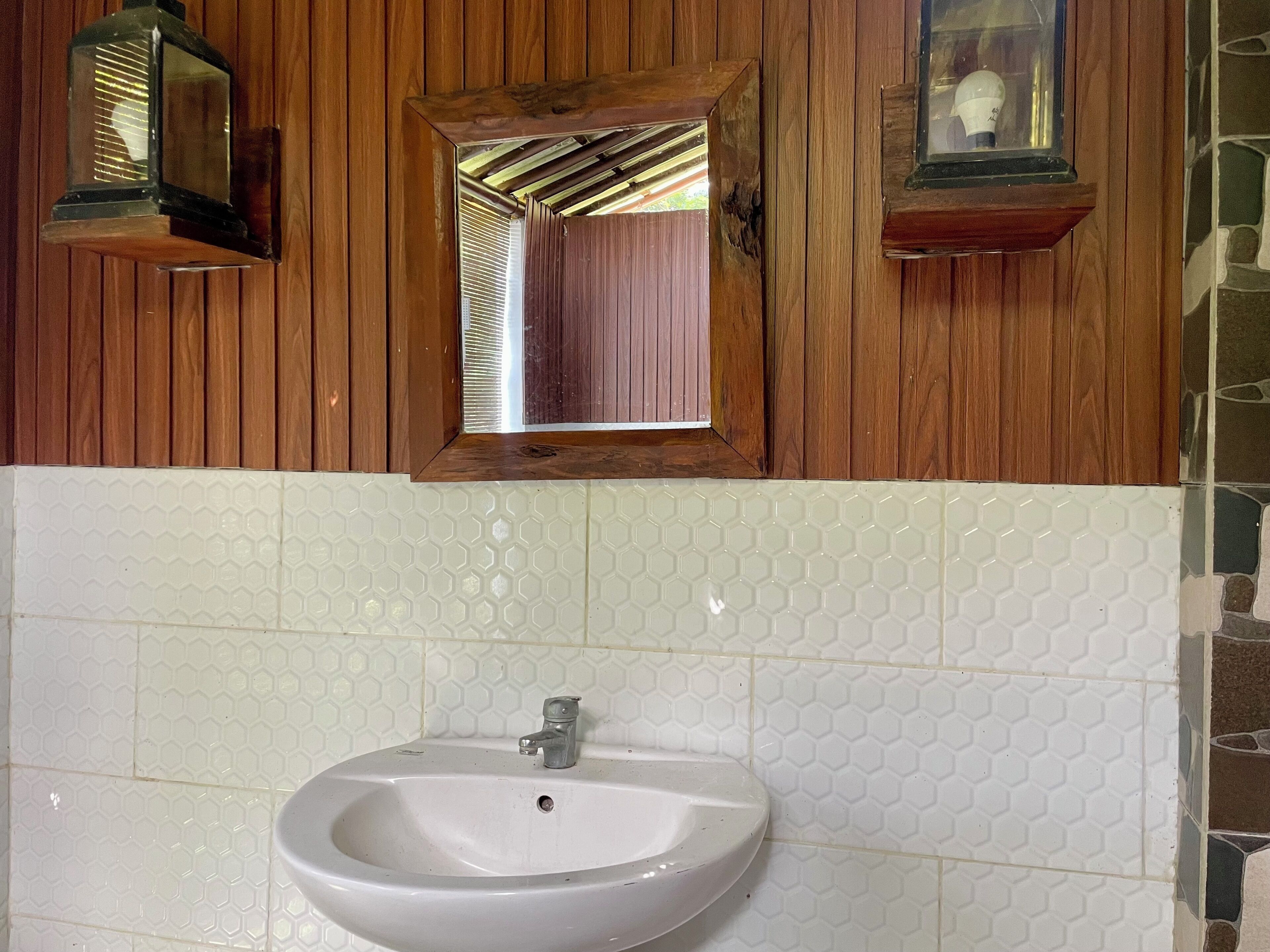 Un baño con pared de madera, un lavamanos blanco y un salpicadero de azulejos hexagonales, y dos luces empotradas.
