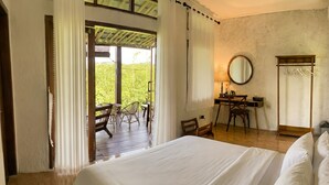 Une chambre avec un grand lit, un bureau et une chaise. Elle possède un balcon avec vue sur la verdure.