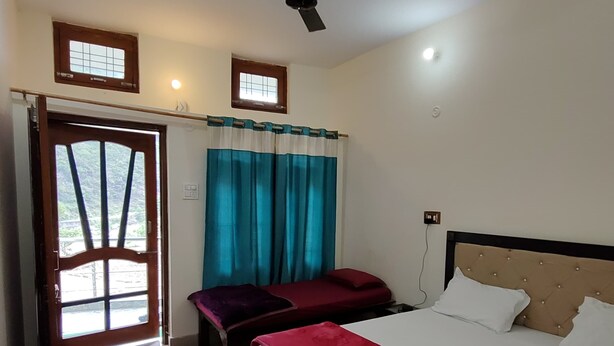 Una camera d'albergo con un letto, un tavolino, una panca, una ventola a soffitto e una finestra con tende.