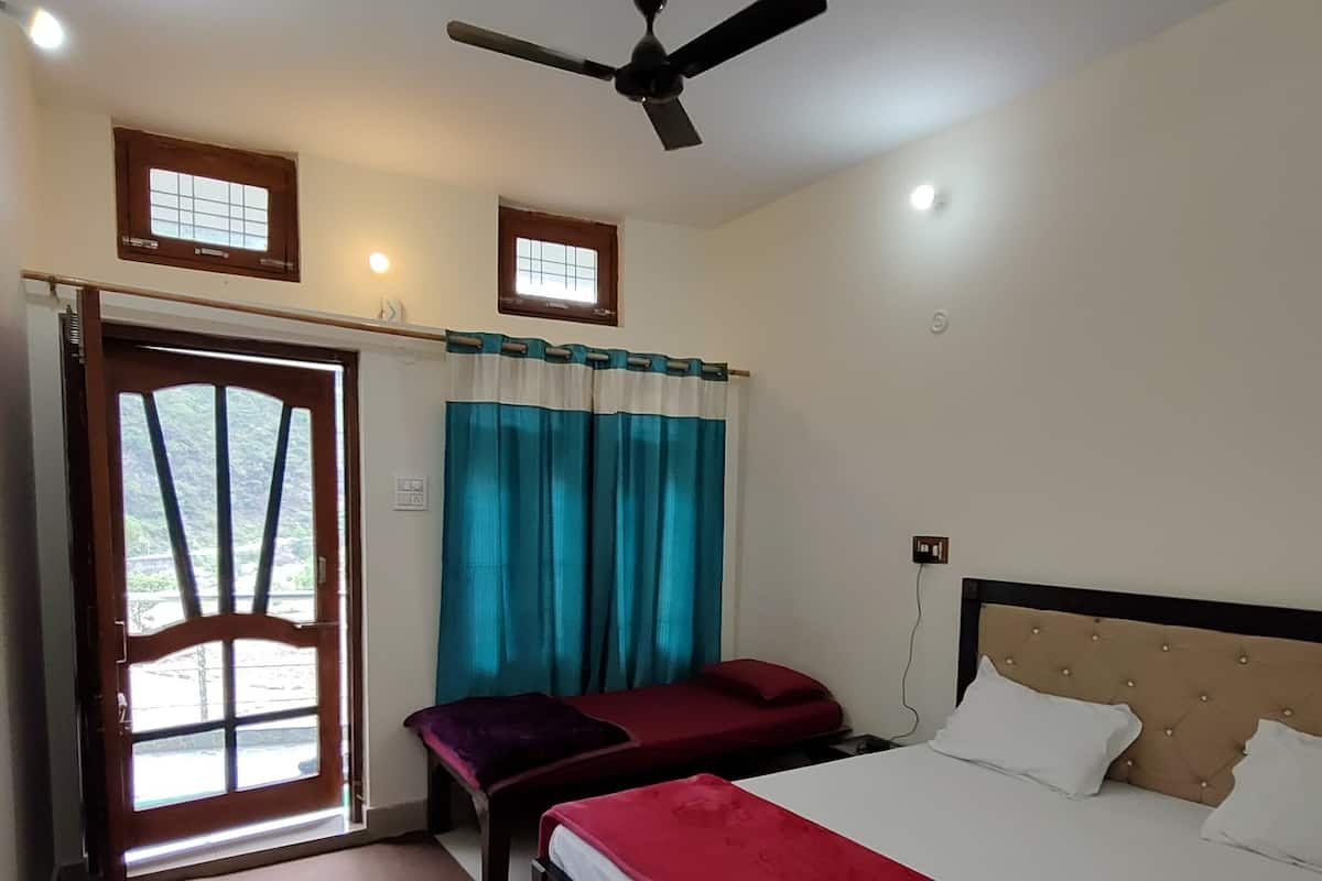 Une chambre d’hôtel avec un lit, une petite table, un banc, un ventilateur de plafond et une fenêtre avec des rideaux.