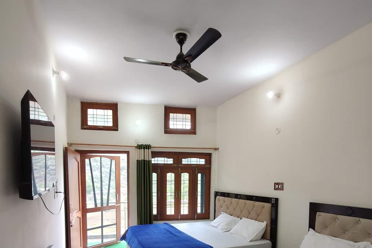 Une chambre d’hôtel avec deux lits, un ventilateur de plafond et une vue sur l’extérieur, visible à travers la porte.