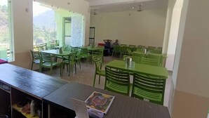 Un'area ristoro con tavoli e sedie verdi, vista sull'esterno e una persona seduta a un tavolo.