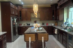 A modern kitchen with dark wood cabinets, a central island with two stools, and a chandelier. - Landy Sweet Home (Richmond)
