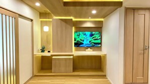 Een modern interieur met een houten vloer, inbouwspots, een flatscreen televisie op een houten voet en een schuifdeur aan de rechterkant.