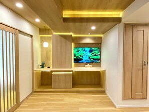 Ein modernes Interieur mit Holzboden, deckenintegrierter Beleuchtung, einem Flachbildfernseher auf einem Holzbodenständer und einer Schiebetür auf der rechten Seite.