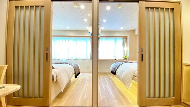 Een hotelkamer met een schuifdeur, twee bedden, een houten vloer en een raam met gordijnen.