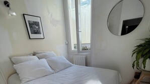 Makuuhuoneessa on suuri sänky, ikkuna, patteri, seinään kiinnitetty valaisin, kehystetty taulu ja ruukussa oleva kasvi.