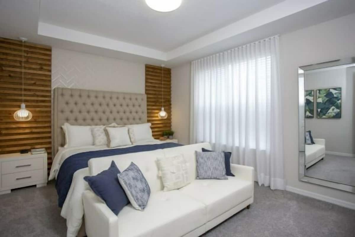 A modern bedroom with a large bed, a white sofa, a mirror, and a wooden accent wall.
